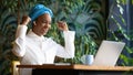 Happy african woman looking at laptop screen, gesturing, cafe interior Royalty Free Stock Photo