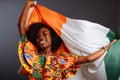 Happy african woman in national clothes smiling and posing with a flag Ivory Coast, C te d`Ivoire isolated over a gray