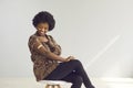 Happy African woman shows arm after jab sitting on chair on copy space studio background