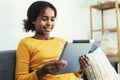 African young girl using digital tablet technology sitting on couch at home Royalty Free Stock Photo