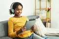 Happy African young girl using digital tablet technology sitting on couch at home Royalty Free Stock Photo