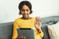 Happy African young girl using digital tablet technology sitting on couch at home Royalty Free Stock Photo