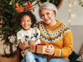 Happy afro american curly boy sitting on grandmother lap with christmas present, smiling at camera Royalty Free Stock Photo