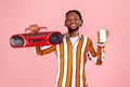 Happy afro-american man with dreadlocks in striped shirt and earphones holding tape recorder and white screen smartphone looking Royalty Free Stock Photo