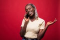 Happy young afro american woman talking on the phone and looking away over red background Royalty Free Stock Photo