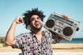 Happy Afro man having fun listening to music with wireless headphones and vintage boombox on the beach during summer Royalty Free Stock Photo
