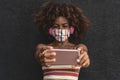 Happy Afro woman taking selfie with mobile smartphone while wearing face colored mask and listening music with headphones
