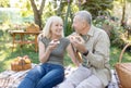 Happy aged couple having picnic in their garden, sitting on blanket and eating toasts with jam, enjoying spring day Royalty Free Stock Photo