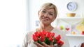 Happy aged female holding bouquet of tulips from admirer and smiling at camera