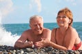 Happy aged pair lie on pebble beach