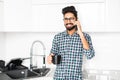 Happy indian young man in checkered shirt talking on cell phone on the kitchen Royalty Free Stock Photo