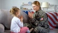 Happy american female soldier and child playing hands on sofa, family time, fun