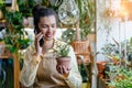 Happy american woman with green plant in florist shop. Proud small business owner takes orders speaks on the phone in Royalty Free Stock Photo