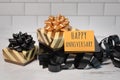 Happy anniversary greetings card sitting on gold and black wrapped gifts ribbon and bows