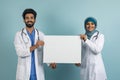 Happy arab doctors in medical uniform and hijab showing blank placard Royalty Free Stock Photo