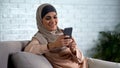 Happy arab female scrolling social networks photo smartphone, housewife leisure Royalty Free Stock Photo