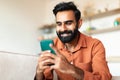 Happy arab guy sitting with smartphone in hands at home Royalty Free Stock Photo