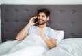 Happy arab guy talking on smartphone, calling somebody in the morning and having cellphone conversation sitting in bed Royalty Free Stock Photo