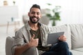 Happy Arab guy using tablet pc, studying or working remotely, having online conference, showing thumb up at home Royalty Free Stock Photo