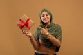 Happy arab woman holding wrapped present box and pointing finger on it, standing over brown background Royalty Free Stock Photo