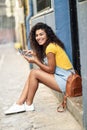 Happy Arab woman sitting on urban step with a digital tablet. African girl wearing casual clothes. Young traveler female with