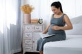 Happy Asia pregnant woman reading book and sitting touching belly on white bed Royalty Free Stock Photo