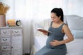 Happy Asia pregnant woman reading book and sitting on white bed Royalty Free Stock Photo