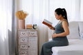 Happy Asia pregnant woman reading book and sitting on white bed Royalty Free Stock Photo