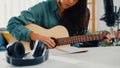 Happy asia woman songwriter play acoustic guitar listen song from smartphone think and write notes lyrics song in paper sit in Royalty Free Stock Photo