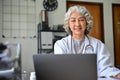 Happy Asian aged female doctor concentrating on her medical research, using laptop Royalty Free Stock Photo