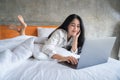 Happy asian beautiful woman working on a laptop sitting on the bed in the house Royalty Free Stock Photo