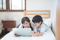 Happy asian boy and girl playing game in laptop lying on bed in bedroom in house,brother and sister using notebook do homework, Royalty Free Stock Photo