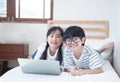 Happy asian boy and girl playing game in laptop lying on bed in bedroom in house,brother and sister using notebook do homework, Royalty Free Stock Photo