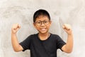 Happy Asian boy with glasses hands up and smiling over grey background. Royalty Free Stock Photo