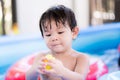 Happy Asian boy is playing a yellow toy in a blue rubber pool. Cute little kid attentively looked at his hand holding a toy. Royalty Free Stock Photo