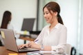 Happy Asian business woman working with laptop and smile looking at camera at modern office Royalty Free Stock Photo