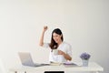 A happy Asian businesswoman is smiling and showing her fists with joy while sitting at her desk Royalty Free Stock Photo