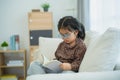 Happy asian child baby girl smiling wearing glasses and reading book while sitting on couch sofa in living room at home. Girl Royalty Free Stock Photo