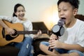 Happy asian child girl,kid boy singing a song together at home,family concert,sister plays the guitar,little brother hold a Royalty Free Stock Photo