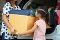 Happy asian child girl and mother helping to carry a cardboard box with stuffs moving into the car together to relocation Royalty Free Stock Photo