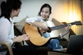 Happy asian child girl playing guitar,online learning,study music on laptop computer,daughter is showing the guitar to her mother