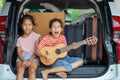 Happy asian child girl playing guitar and singing a song with her sister in a car trunk