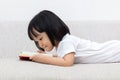 Happy Asian Chinese little girl laying on sofa with book Royalty Free Stock Photo