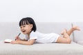 Happy Asian Chinese little girl laying on sofa writing book Royalty Free Stock Photo