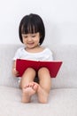 Happy Asian Chinese little girl sitting on sofa with book Royalty Free Stock Photo