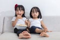 Happy Asian Chinese little sisters eating popcorn on the sofa