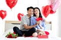 Happy Asian couple holding red heart and hugging each other while sitting on white bed in bedroom, romantic lover celebrating Royalty Free Stock Photo