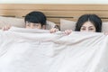 Asian couple lying in bed peeking out from under the blanket and looking at camera. funny couple relaxing in bedroom Royalty Free Stock Photo
