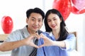 Happy Asian couple making heart shape hands while sitting on bed in beautifully decorated bedroom with red balloons, romantic Royalty Free Stock Photo