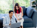 Happy Asian couple, man sit on floor and young woman on sofa, looking and using laptop computer. Royalty Free Stock Photo